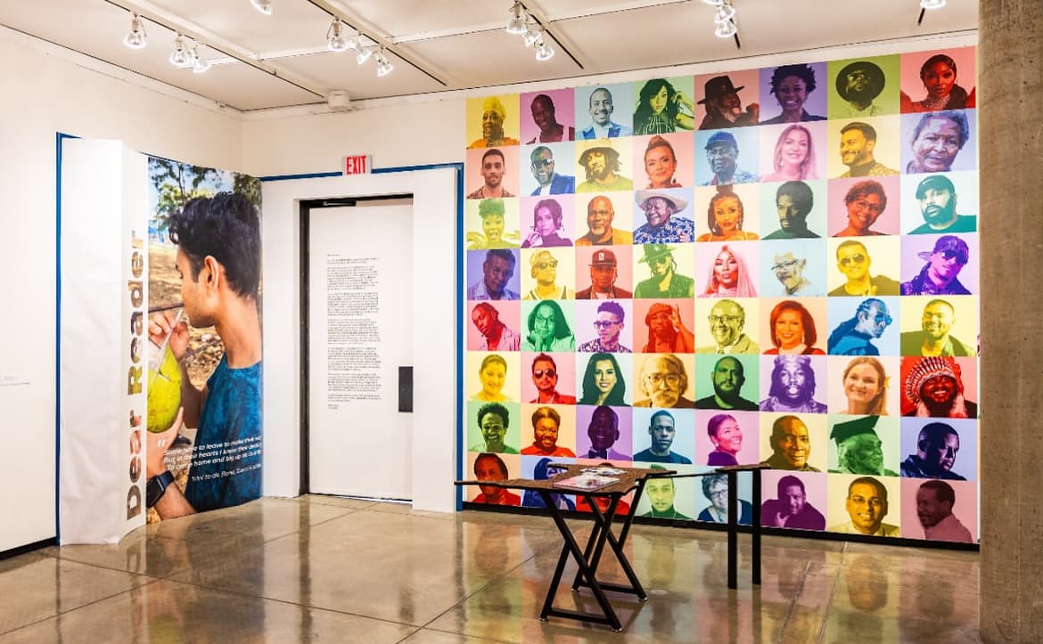Complete Dis Is We People installation showing wall of portraits and Trinidad-shaped table