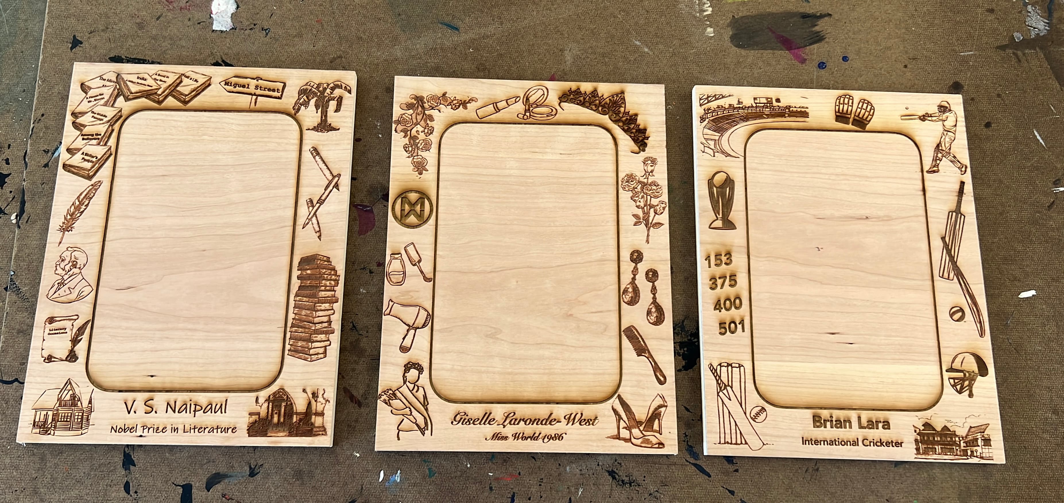Laser-engraved wooden frames showing custom border designs for V.S. Naipaul, Giselle Laronde-West, and Brian Lara